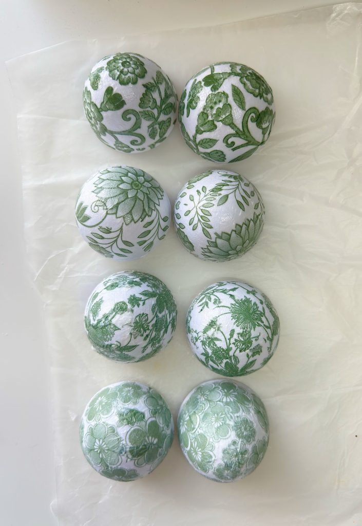 Eight round white objects with green floral patterns are arranged in two columns and four rows on a sheet of wax paper.