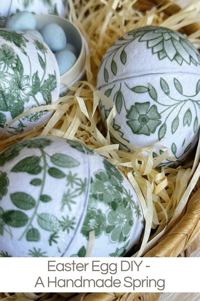 A close-up of decorative Easter eggs with green floral patterns placed in a basket filled with straw, next to a small bowl of blue candy eggs. Text reads: "Easter Egg DIY - A Handmade Spring.