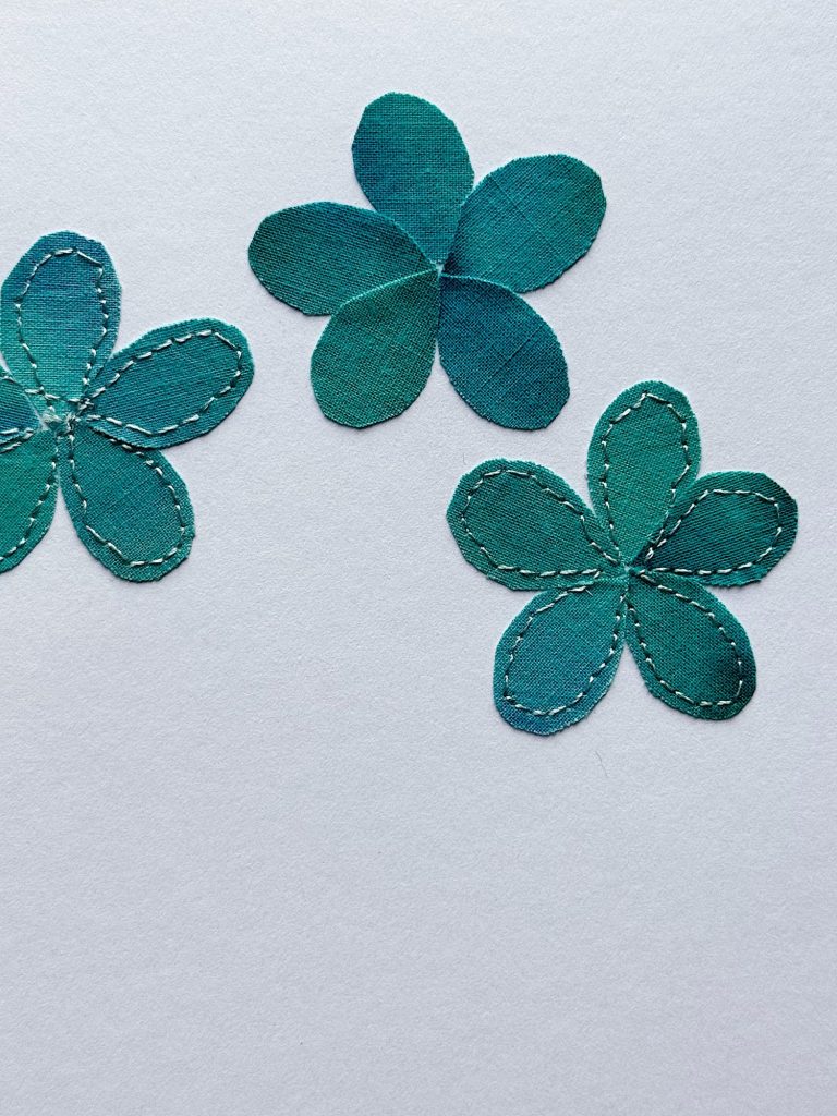 Three teal fabric flower shapes with visible stitched outlines are arranged on a plain light background.