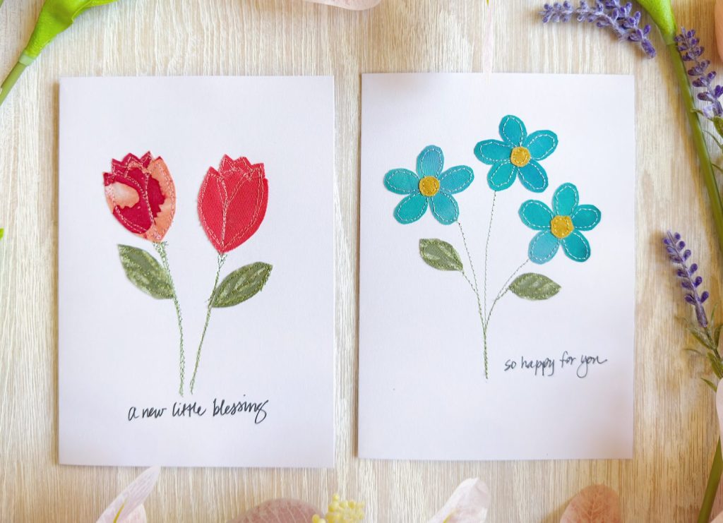 Two greeting cards with fabric flower designs; the left card has red tulips and reads "a new little blessing," the right card has blue daisies and reads "so happy for you.