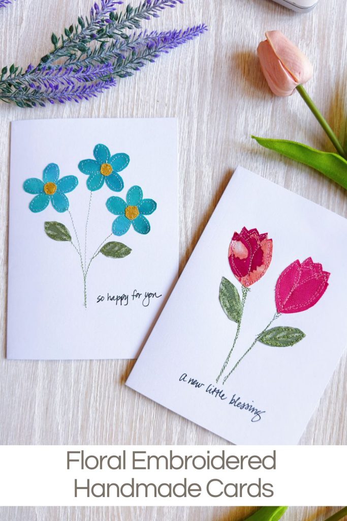 Two handmade greeting cards with embroidered flowers are displayed on a tabletop, one with blue daisies and the other with red tulips. Flowers and greenery are arranged around the cards.