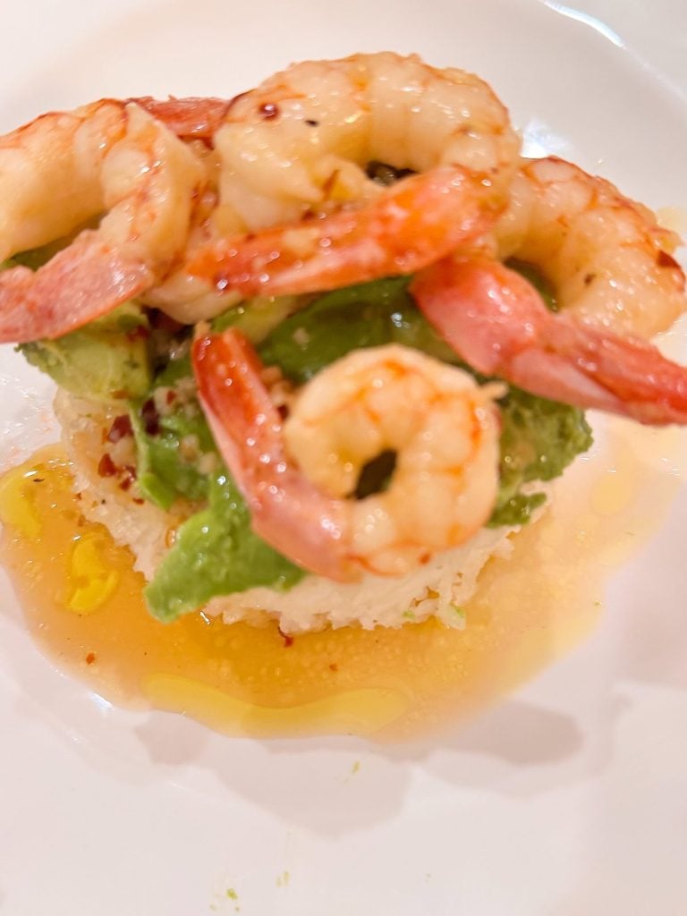 A close-up of cooked shrimp on a bed of avocado and rice, drizzled with oil, served on a white plate.