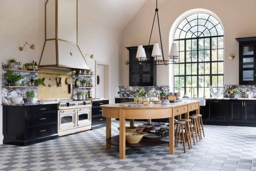 Spacious kitchen with checkered tile floor, large arched window, black cabinets, marble backsplash, wooden island with stools, and white and gold range.
