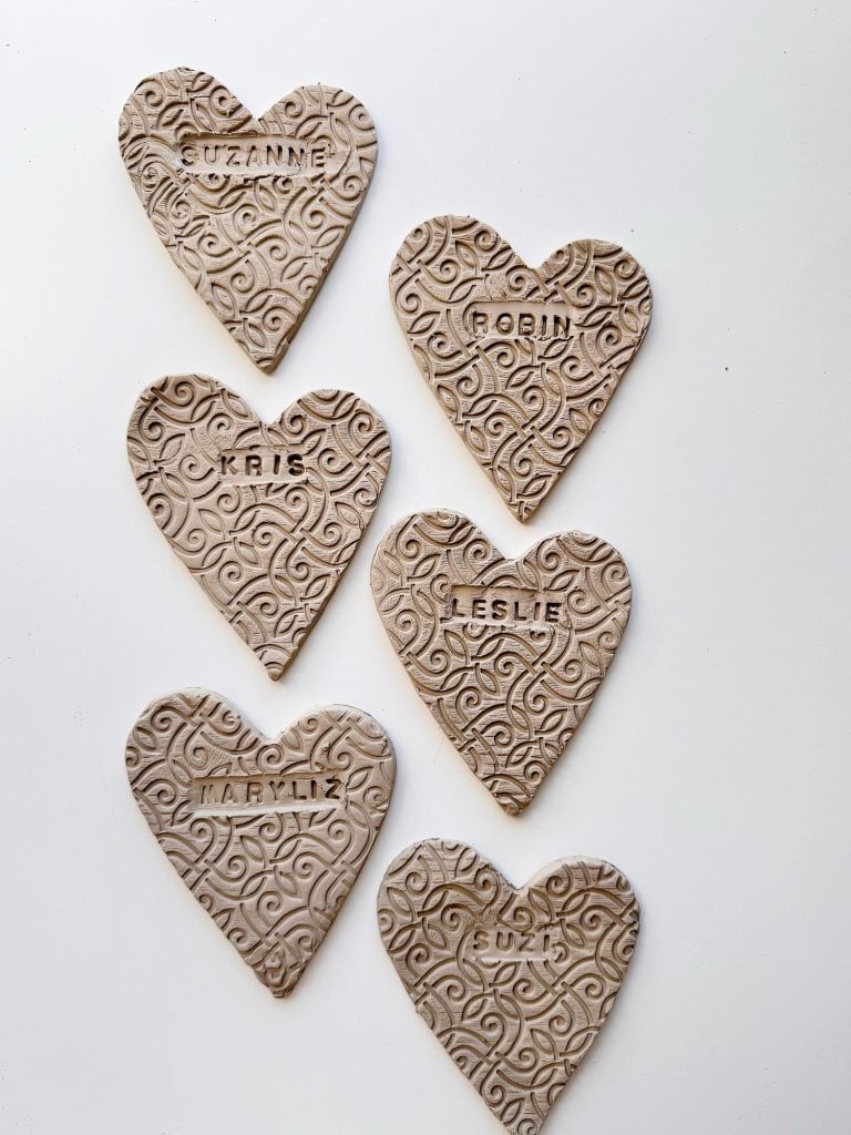 Six heart-shaped clay ornaments with intricate swirl patterns, each labeled with a different name: Suzanne, Robin, Kris, Leslie, Maryliz, and Suzi.