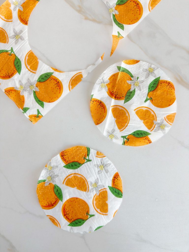 Three circular pieces of paper with orange and leaf patterns, and one cut-out section, are placed on a white surface.