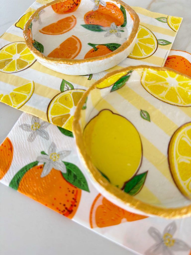 Two ceramic bowls with orange and lemon designs are placed on paper napkins decorated with citrus fruit patterns.
