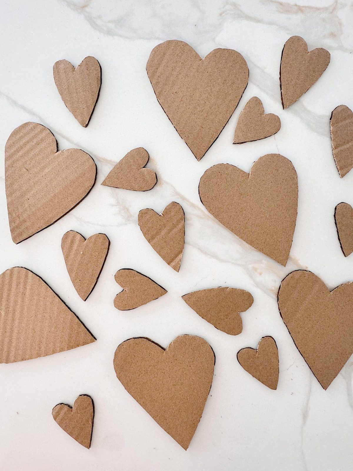Several cardboard hearts of different sizes are scattered on a white marble surface.
