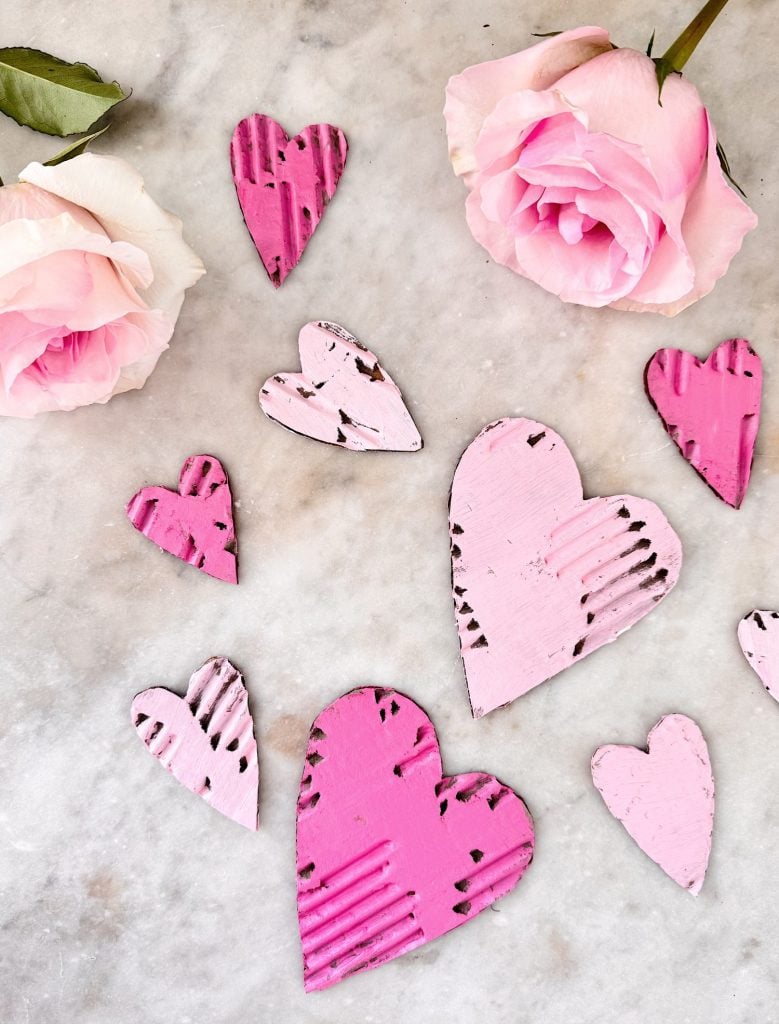 Pink and white roses next to several pink painted wooden heart shapes on a marble surface.