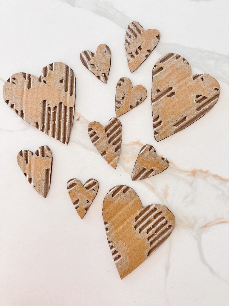 Several heart shapes cut from corrugated cardboard are arranged on a white marble surface.