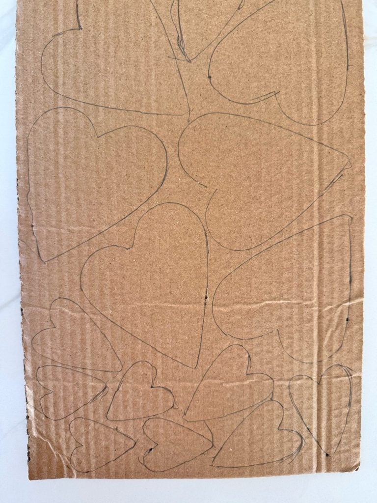 A piece of cardboard with multiple heart shapes of varying sizes drawn on it with black marker.