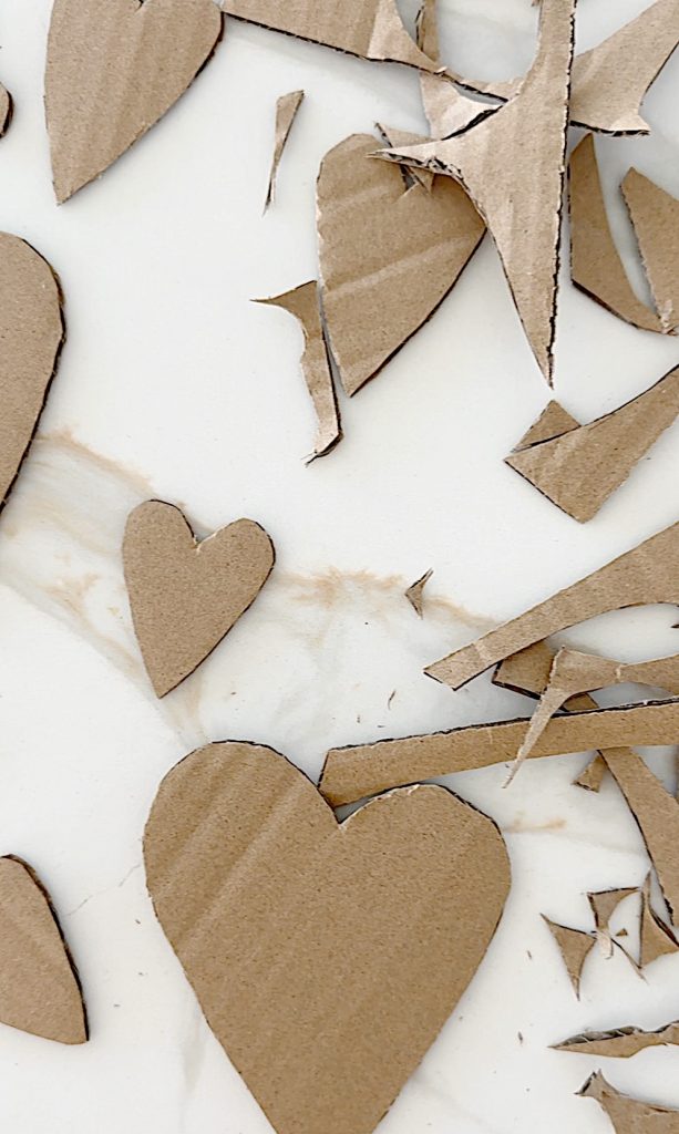 Cardboard hearts and scraps are scattered on a white marble surface.