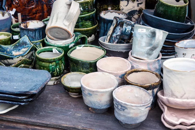 A variety of handmade ceramic mugs, cups, and bowls in different shapes and colors displayed on a wooden surface.
