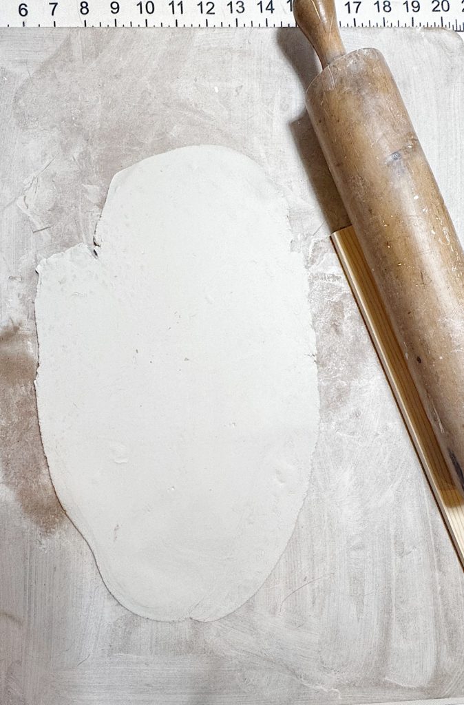 Rolled out dough on a floured surface next to a wooden rolling pin, with a ruler at the top edge of the image.
