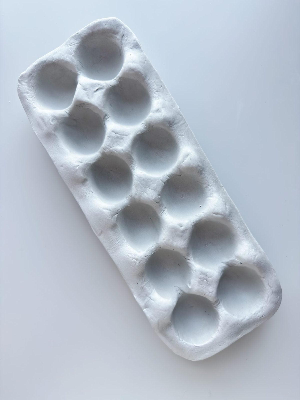 A handmade white clay tray with ten round indents arranged in two rows of five, placed on a plain white surface.