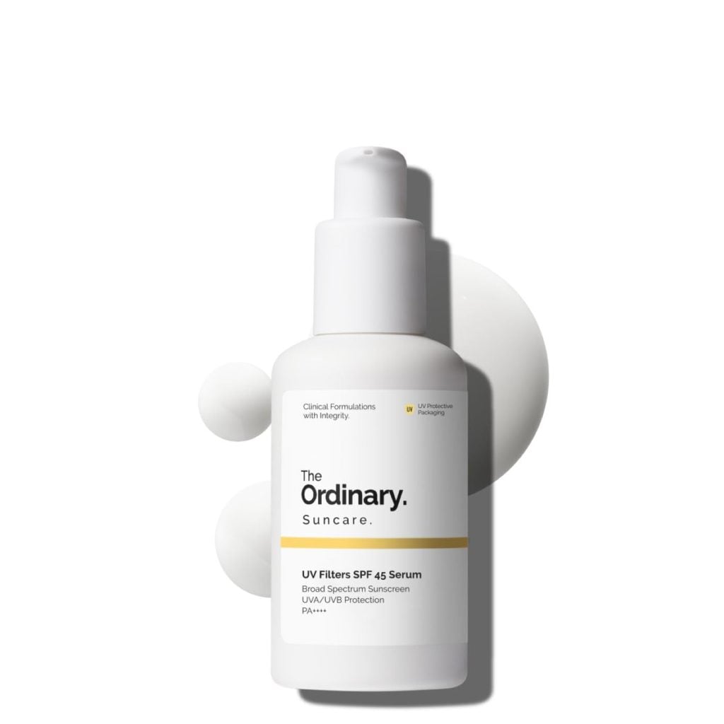 A white bottle of The Ordinary Suncare UV Filters SPF 45 Serum with a pump dispenser, shown against a white background with drops of the product nearby&mdash;perfect for grabbing during the Amazon Big Spring Sale.