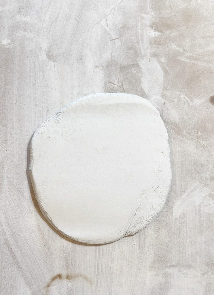 A round, flat disc of white dough rests on a lightly floured surface.