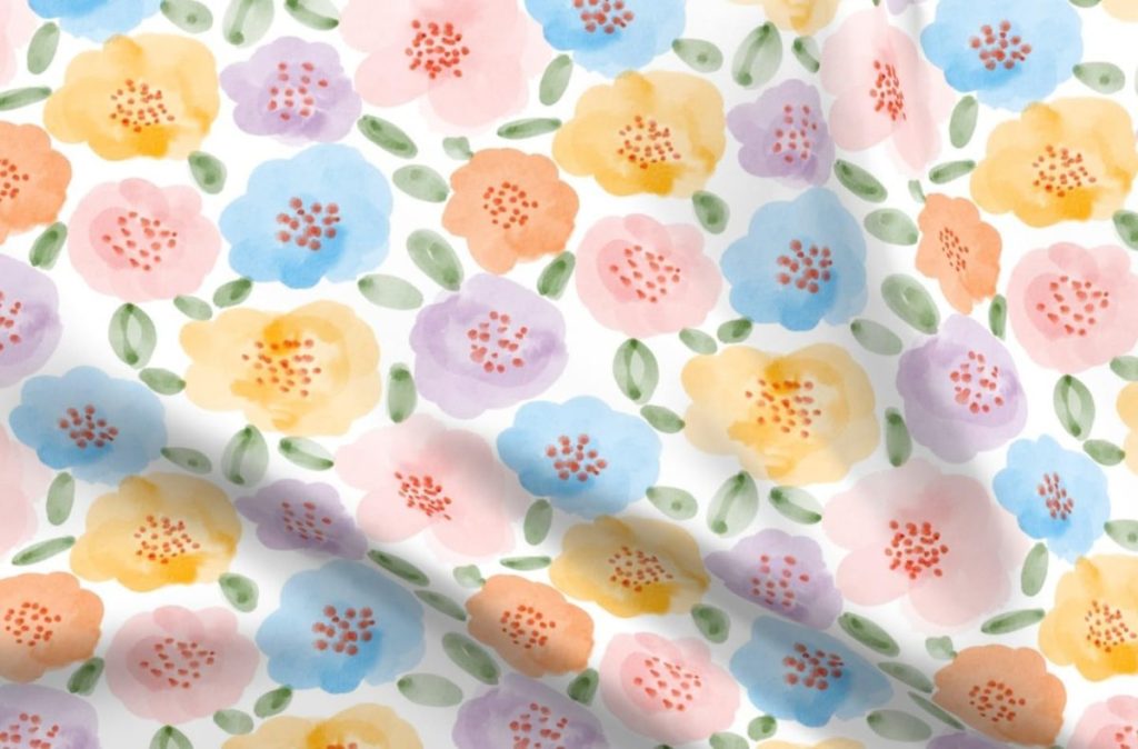 A fabric with a watercolor floral pattern featuring yellow, pink, orange, and blue flowers with green leaves on a white background.