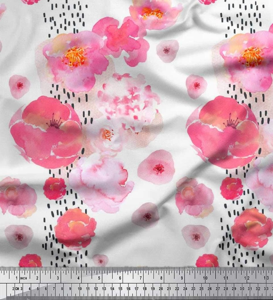 A fabric with a watercolor floral pattern in pink and peach hues, scattered with vertical black dash marks, shown with a measuring ruler along the bottom edge.