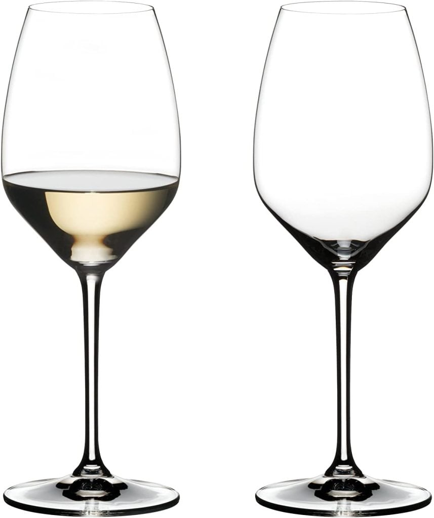 Two clear, empty wine glasses; the left glass is filled halfway with white wine, while the right glass is empty. Both glasses are shown against a plain white background.