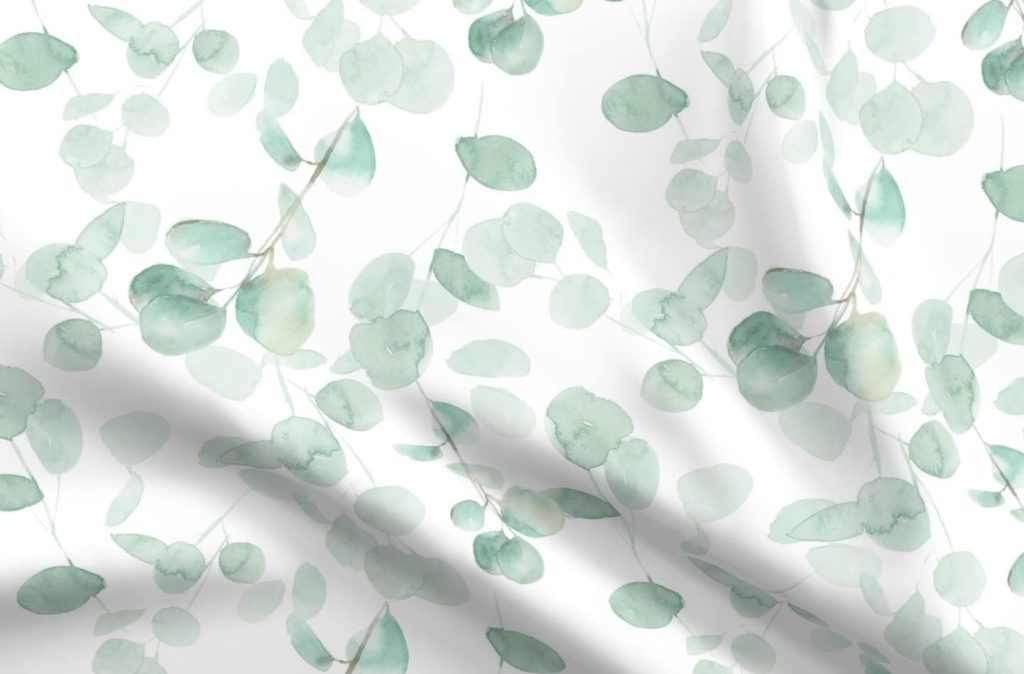 Watercolor-style green eucalyptus leaves pattern on a white fabric background with soft folds and gentle shadows.