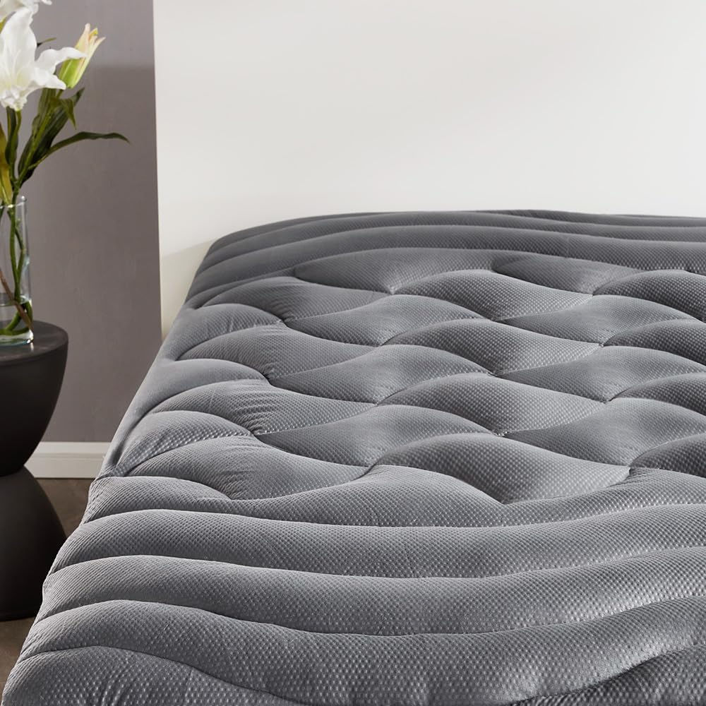 A close-up view of a gray air mattress with a textured, quilted surface in a modern, inspired home bedroom; a small black side table with white flowers sits beside it.