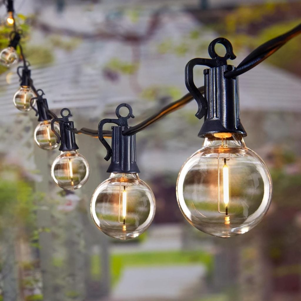 Close-up of several round outdoor string lights with black fixtures, softly glowing in a row against a blurred garden background&mdash;perfect for sprucing up your space during the Amazon Big Spring Sale.