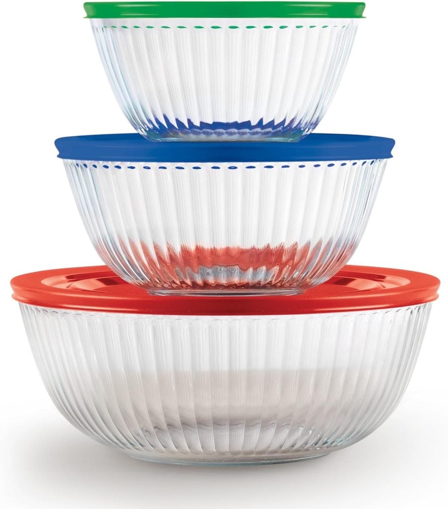 Three clear ribbed glass bowls stacked, each with a differently colored lid: green on top, blue in the middle, and red on the bottom.
