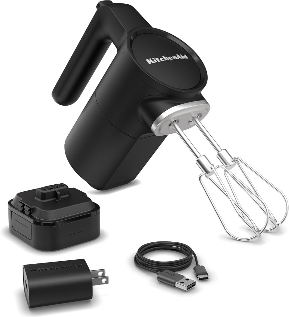 A black KitchenAid cordless hand mixer with two beaters, a rechargeable battery pack, power adapter, and USB charging cable is arranged on a white background&mdash;perfect for upgrading your kitchen during the Amazon Big Spring Sale.