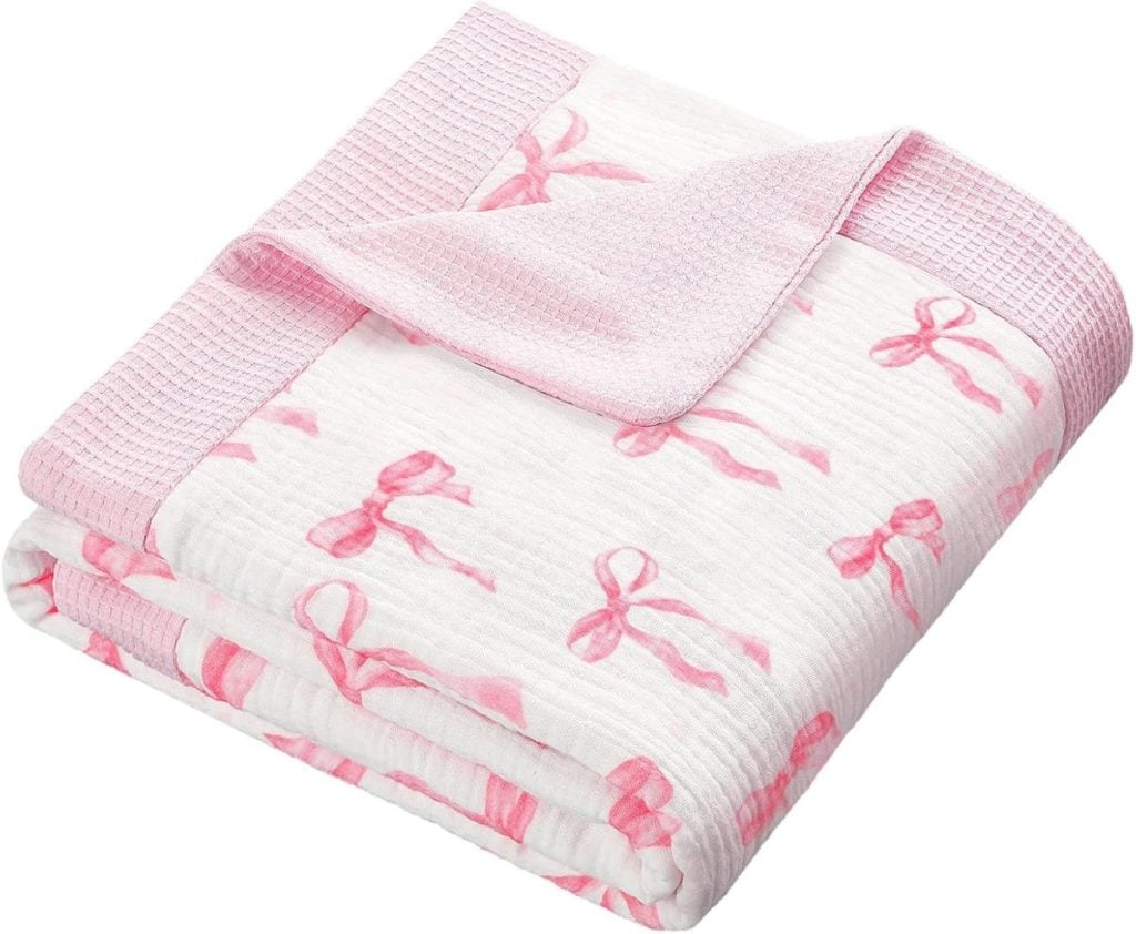A folded baby blanket with a pink trim and pink bow pattern on a white background.