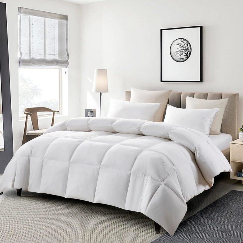 A neatly made bed with a white comforter and four pillows in a modern bedroom with light walls, a window, a chair, and framed wall art&mdash;perfect inspiration for your next refresh during the Amazon Big Spring Sale.