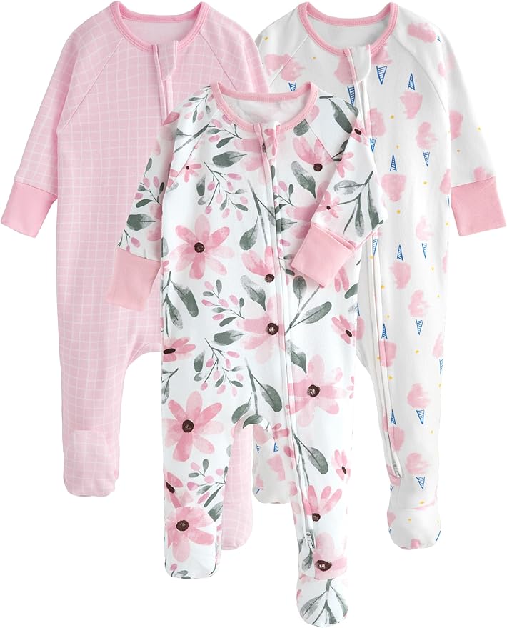 Three baby footed onesies with zippers are shown: one pink with a grid pattern, one white with pink floral print, and one white with small colorful shapes.