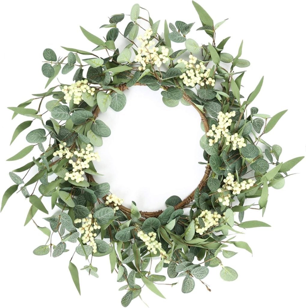A circular wreath made of green leaves and small white berries, arranged in a natural, decorative style.