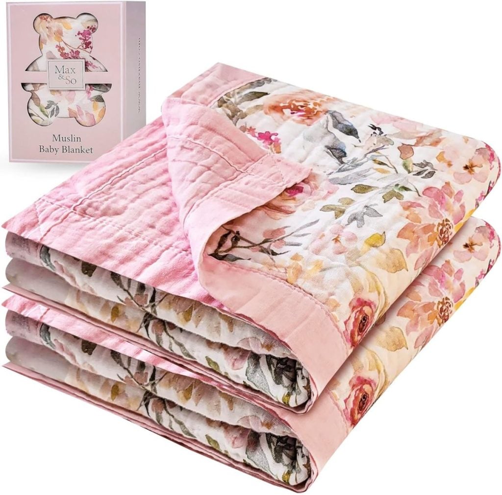 A folded pink and floral muslin baby blanket is displayed next to its packaging box labeled "Max and So Muslin Baby Blanket.