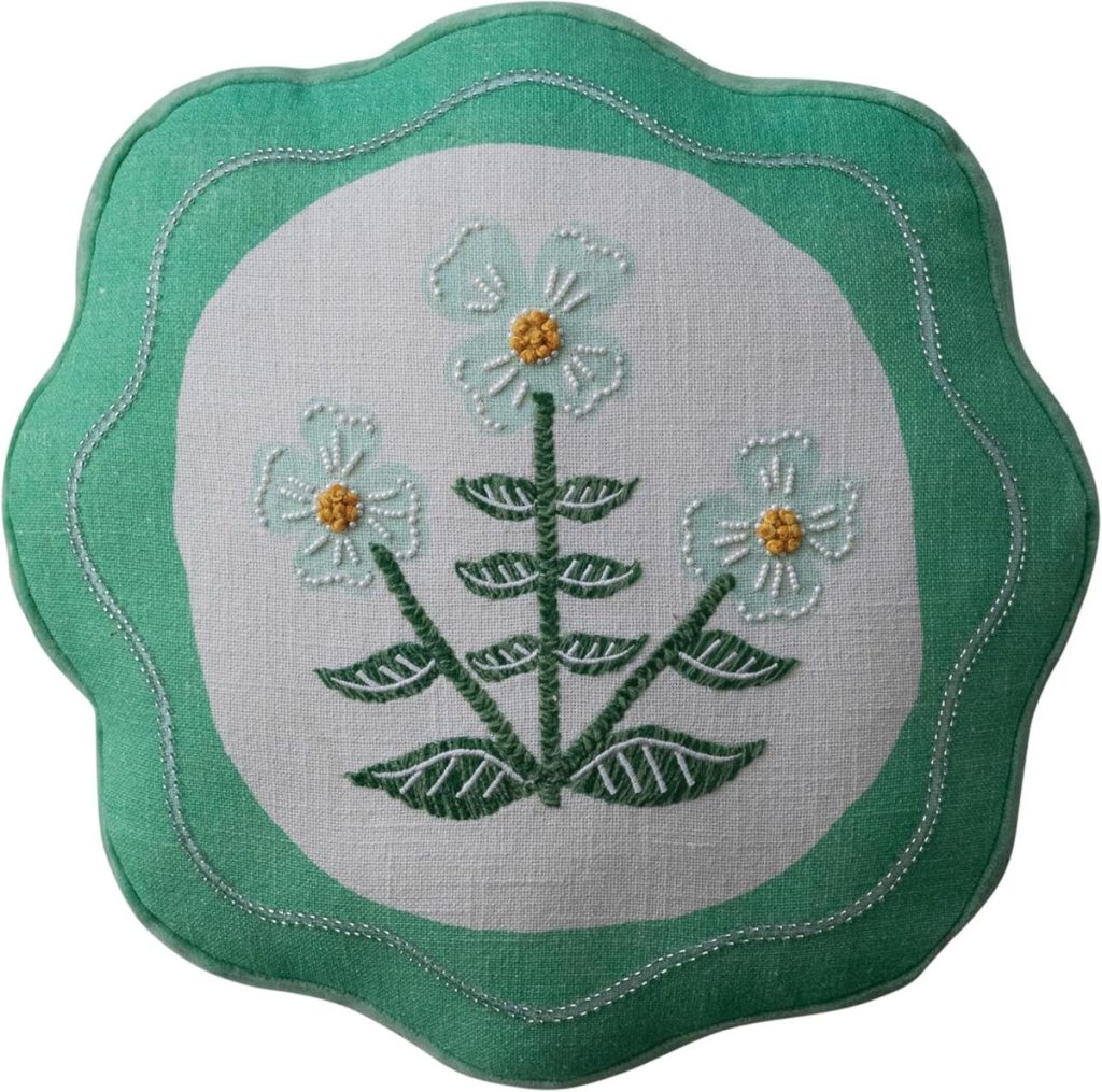 Scalloped green pillow featuring an embroidered design of three white flowers with yellow centers and green stems and leaves.