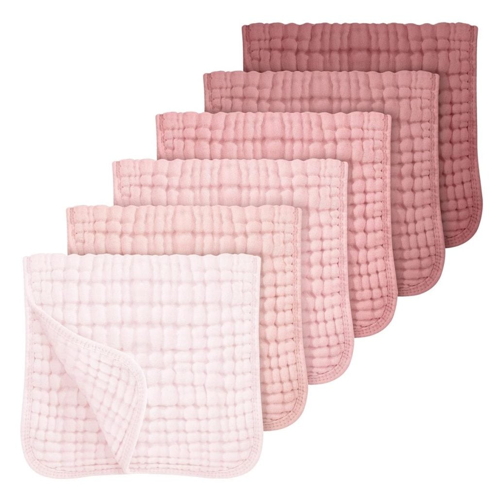 Six pink muslin washcloths are arranged in a row, each featuring a quilted texture and two layers. The shades range from light pink in front to darker pink in the back.