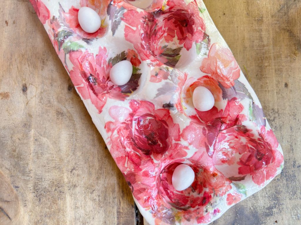 A floral-patterned egg tray holding five white eggs sits on a wooden surface.
