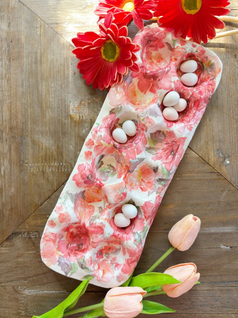 A floral-patterned egg tray holding small white eggs, with red daisies and pink tulips arranged on a wooden surface.