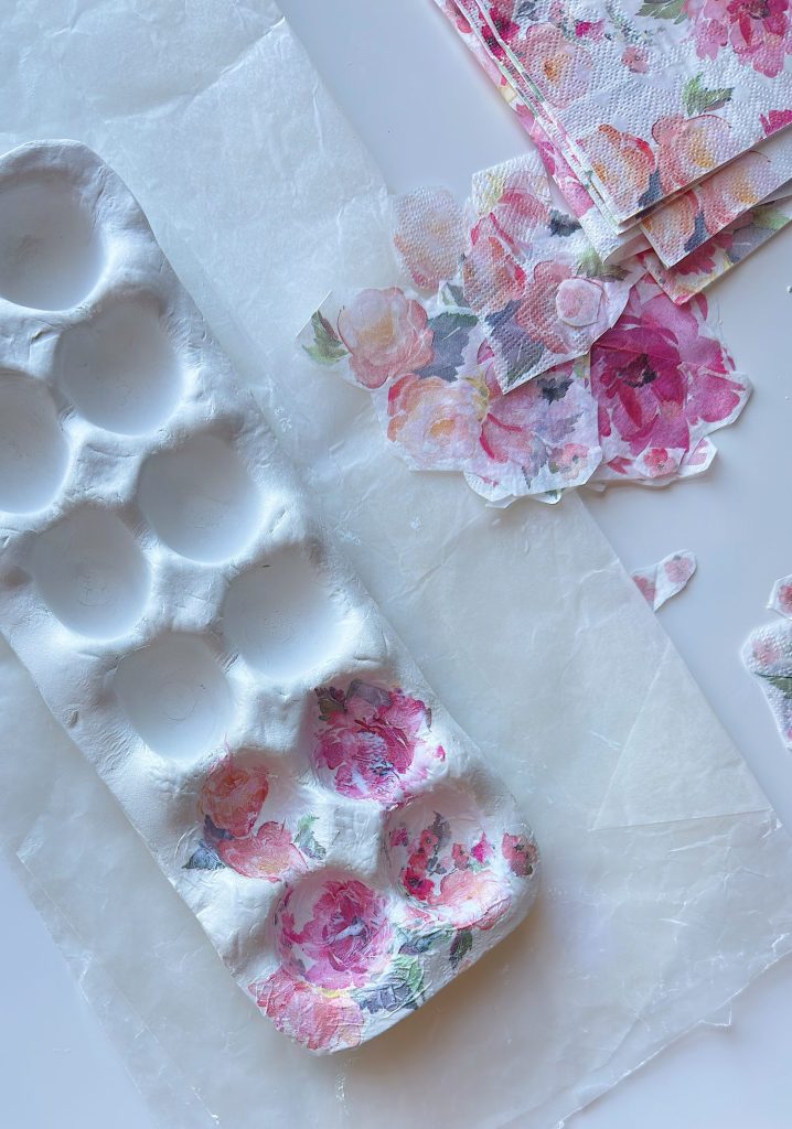 A white paint palette decorated with floral-patterned napkin pieces, with additional floral napkins and wax paper on the table.