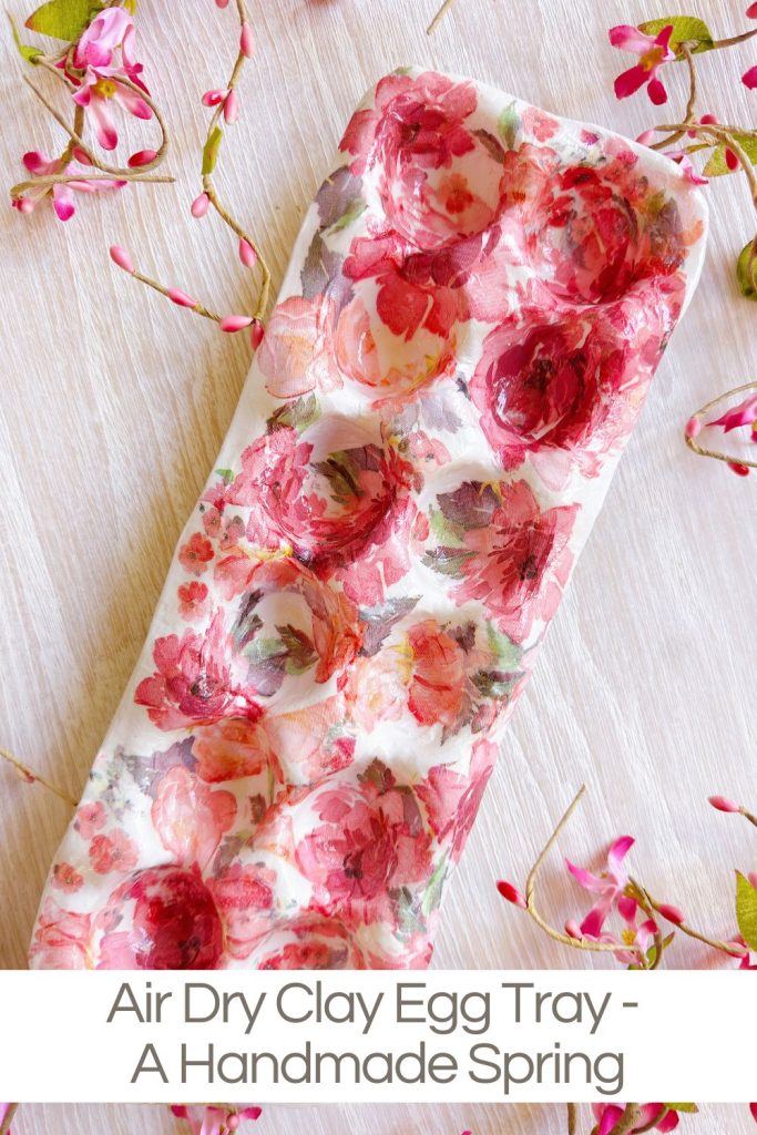 A handmade air dry clay egg tray with a pink and red floral pattern, surrounded by small pink flower petals on a light wooden surface.