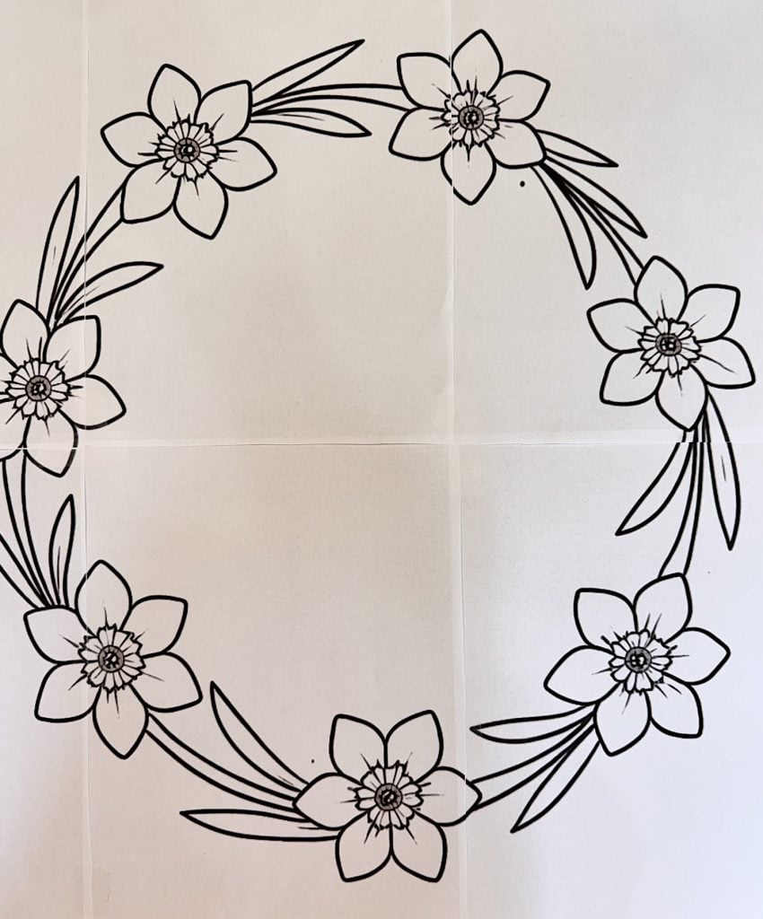 A black and white illustration of a circular floral wreath with six flowers and leaves evenly spaced around the ring.