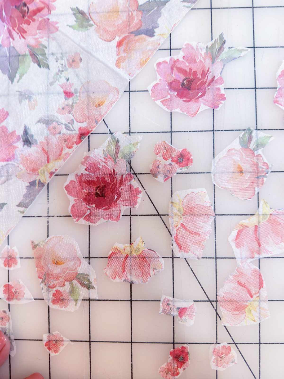 Floral patterned paper is cut into various flower shapes and arranged on a grid cutting mat.