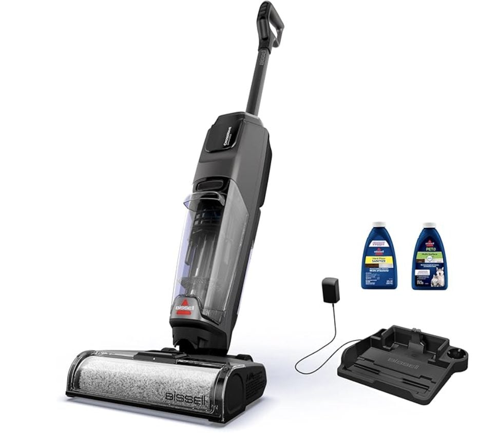 A Bissell cordless vacuum cleaner with a charging base, two bottles of cleaning solution, and a power adapter displayed beside it&mdash;perfect for tackling spring cleaning during the Amazon Big Spring Sale.