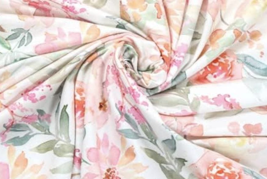 A close-up of fabric with a pastel floral print in pink, orange, green, and white, arranged in a swirl.