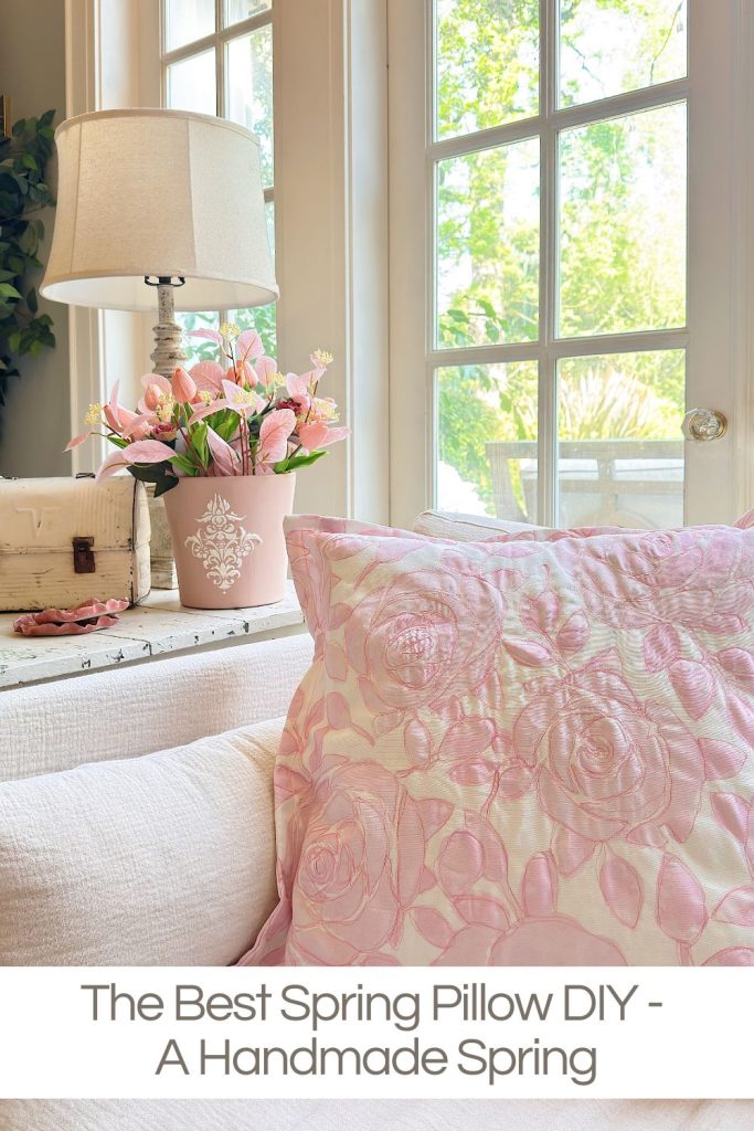 A pink floral pillow on a white couch, next to a lamp and a pot of pink flowers, with sunlight streaming through large windows. Text reads: "The Best Spring Pillow DIY - A Handmade Spring.