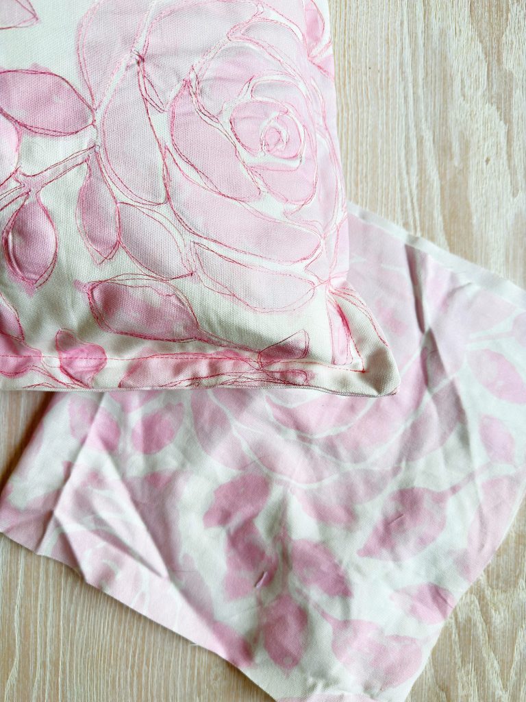 A close-up of a pillow and cloth with light pink floral patterns on a pale wooden surface.