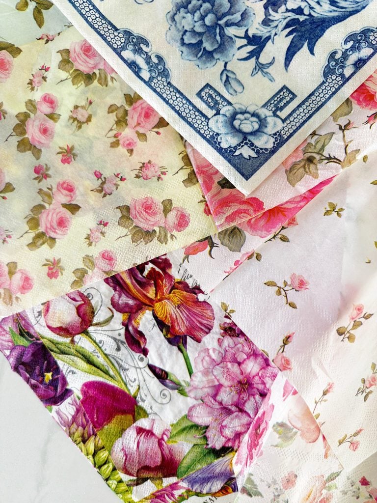 Four paper napkins with different colorful floral patterns are arranged overlapping each other on a white surface.
