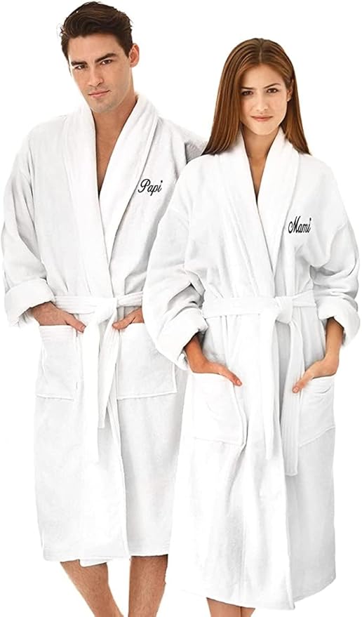 A man and a woman wearing matching white bathrobes embroidered with "Papi" and "Mami" on the chest, perfect for couples searching for a unique name for your home, standing side by side.
