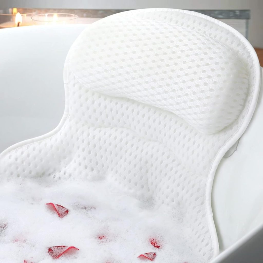 A white textured bath pillow and mat in a bathtub with bubbles and rose petals, with candles in the background&mdash;an ideal setting for relaxation and thoughtful Mother's Day gifts from Amazon.