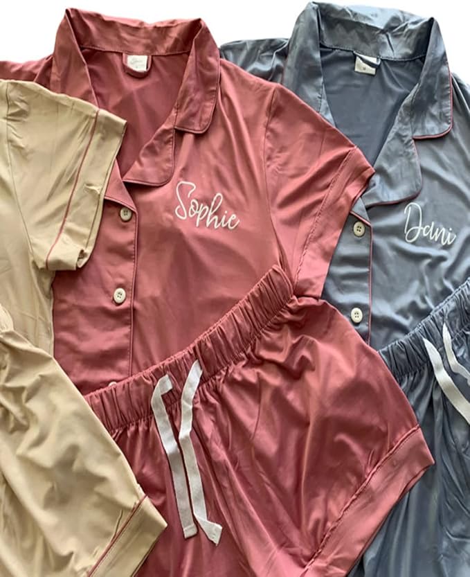 Three sets of short-sleeve button-up pajamas in beige, pink, and gray, each with a name embroidered on the chest: Sophie on pink, Dani on gray.