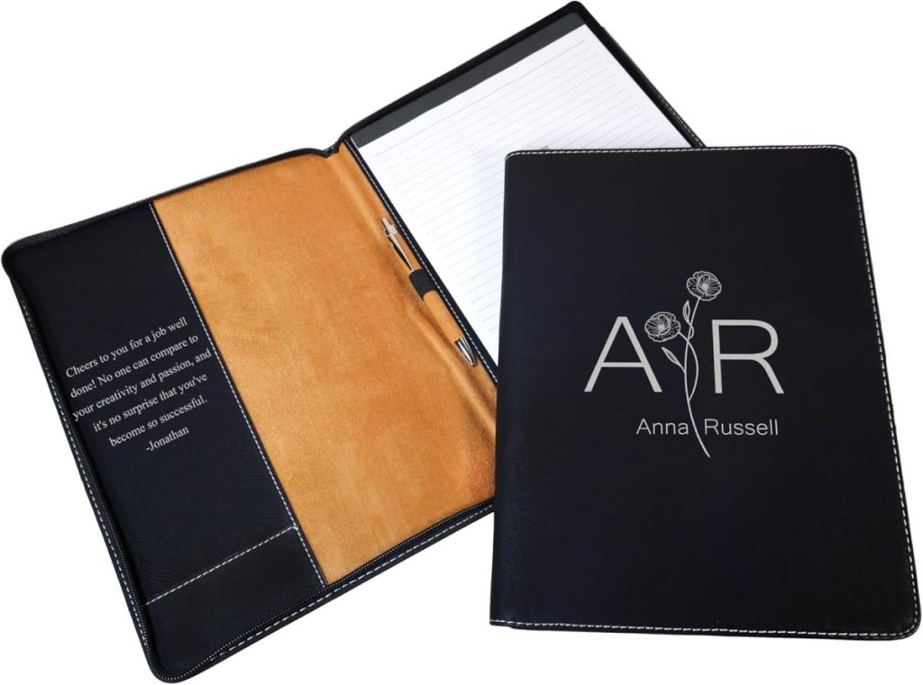 A black leather portfolio with "AR Anna Russell" and two roses on the cover, shown open with a notepad, pen holder, and an inspirational quote on the inside pocket.